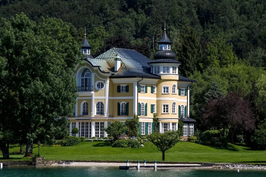 Ein großes gelbes Herrenhaus mit mehreren Türmchen und Bogenfenstern steht an einer Uferpromenade auf Mallorca, umgeben von üppigen Bäumen und viel Grün.