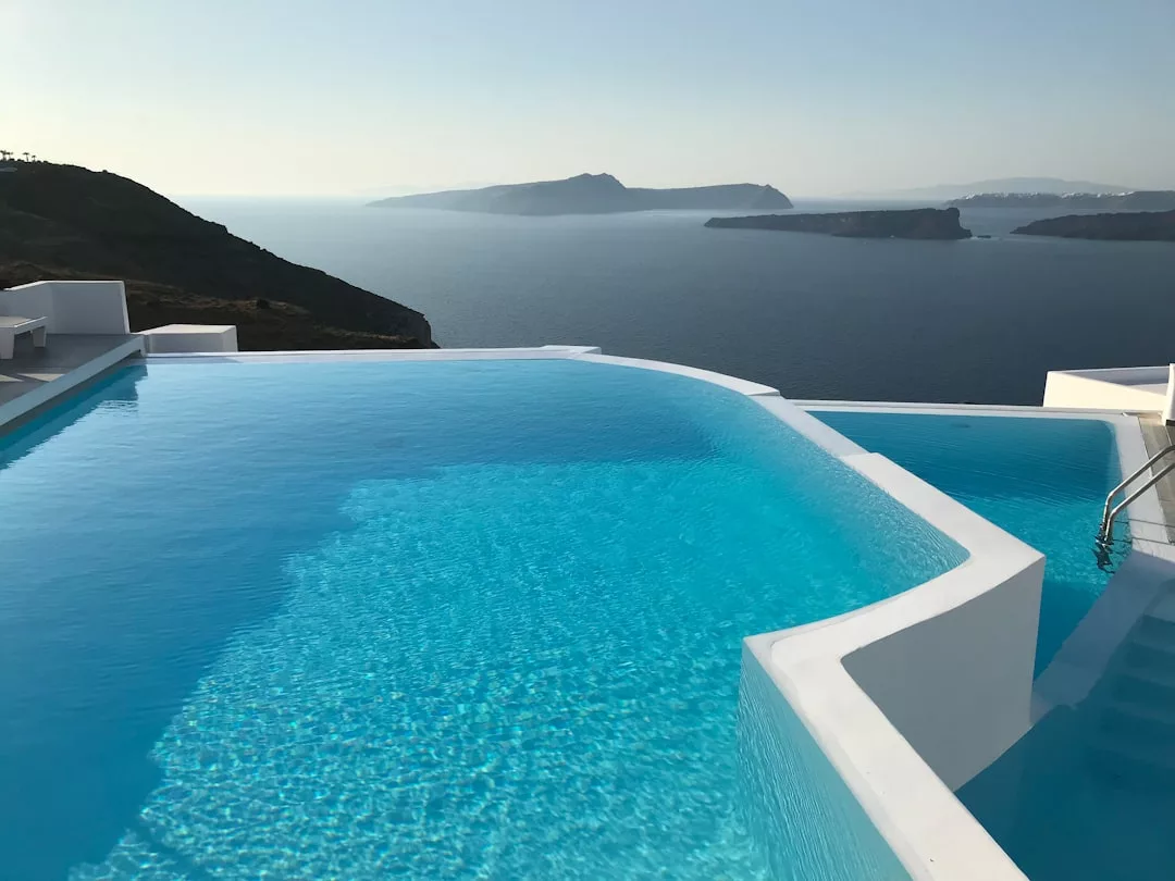 Infinity-Pool mit klarem, blauem Wasser und Blick auf das Meer und die fernen Inseln, umgeben von weißer Architektur unter einem klaren Himmel von Mallorca.