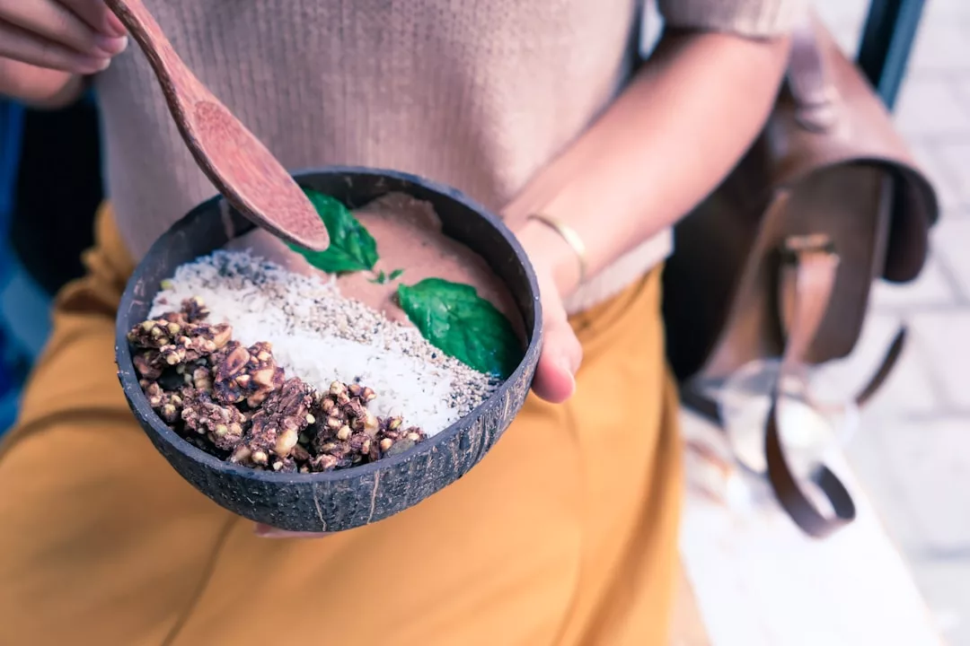 Eine Person auf Mallorca hält eine Kokosnussschale mit einem Smoothie, garniert mit gepufften Körnern, Chiasamen, Kokosraspeln und grünen Blättern, und rührt vorsichtig mit einem Holzlöffel um.