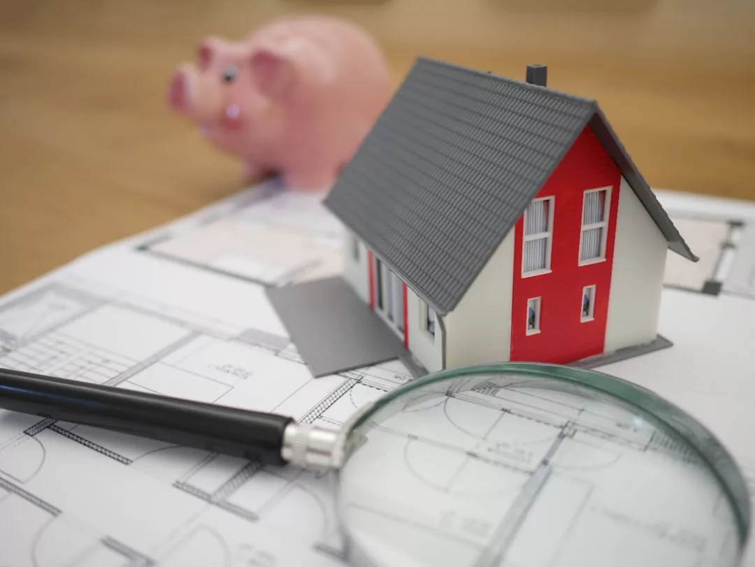 Ein Modellhaus, eine Lupe und ein Sparschwein werden auf Architekturpläne gelegt und fangen die Essenz der Planung Ihrer Traumimmobilie auf Mallorca ein.
