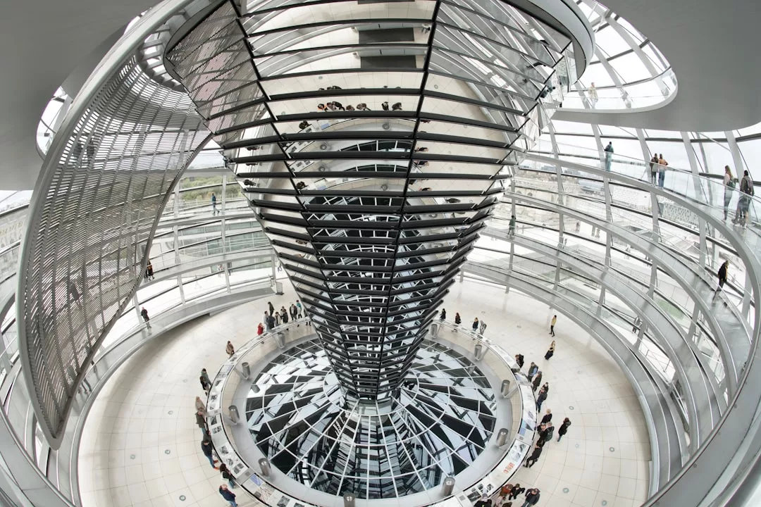 Innenansicht der Reichstagskuppel in Berlin, wo Besucher spiralförmige Rampen entlanggehen und unter einem Glasdach die Spiegelungen auf dem zentralen Spiegelkegel bewundern können – ein auffälliger Kontrast zur sonnendurchfluteten Architektur Mallorcas.