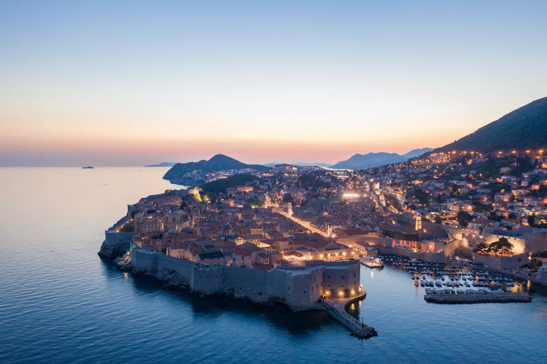 Luftaufnahme der Altstadt von Dubrovnik, umgeben von Steinmauern bei Sonnenuntergang, mit leuchtenden Gebäuden und einem im Hintergrund schimmernden Adriameer – ein Charme, der an die Küstenlandschaft Mallorcas erinnert.