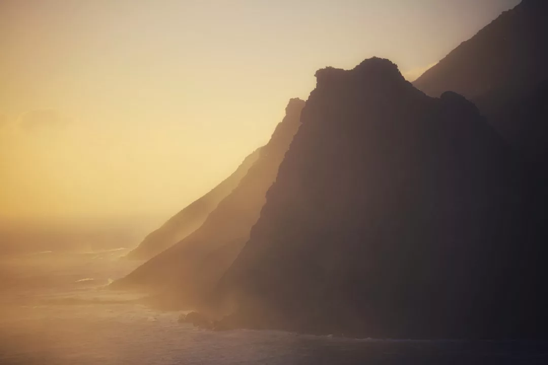 Die steilen Küstenklippen Mallorcas erheben sich über dem Meer und werden am frühen Morgen oder späten Nachmittag von sanftem, goldenem Sonnenlicht und Nebel beleuchtet.