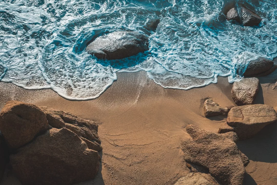 Von oben gesehen spülen Wellen über große Felsen und den Sandstrand auf Mallorca.