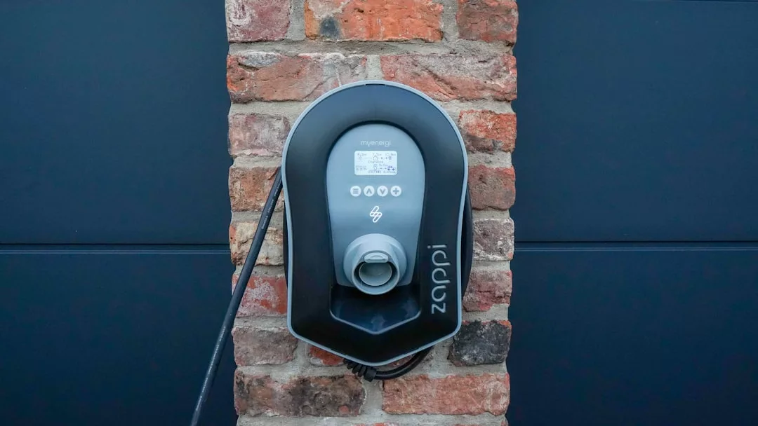 Eine wandmontierte Ladestation für Elektrofahrzeuge mit Display und Kabel, nahtlos an einer Ziegelwand installiert – perfekt für Mallorcas umweltfreundliche Häuser.