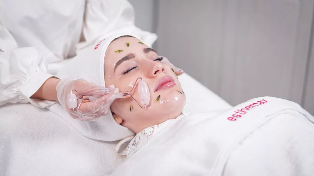Eine Person, die auf einer Spa-Liege auf Mallorca liegt, erhält eine Gesichtsbehandlung mit einem Jaderoller und Pflastern im Gesicht, betreut von einer Person mit Handschuhen.