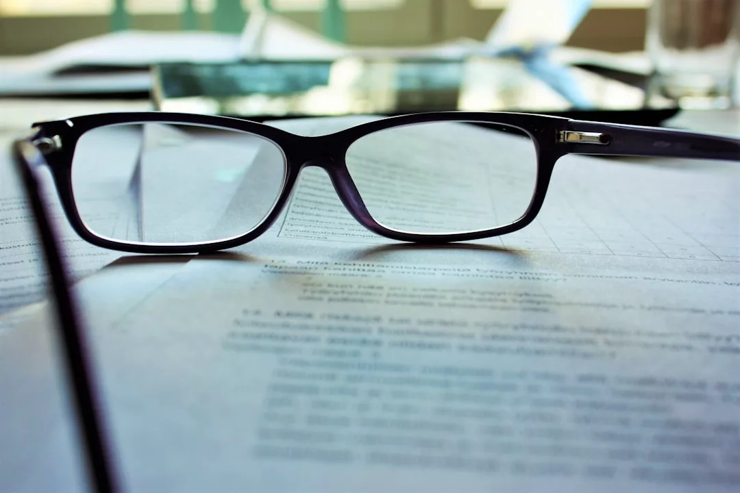 Eine schwarze Brille liegt auf gedruckten Dokumenten auf einem Schreibtisch und erinnert an die ruhige Konzentration eines Mallorca-Morgens, mit weiteren Papieren und einem Glas im Hintergrund.