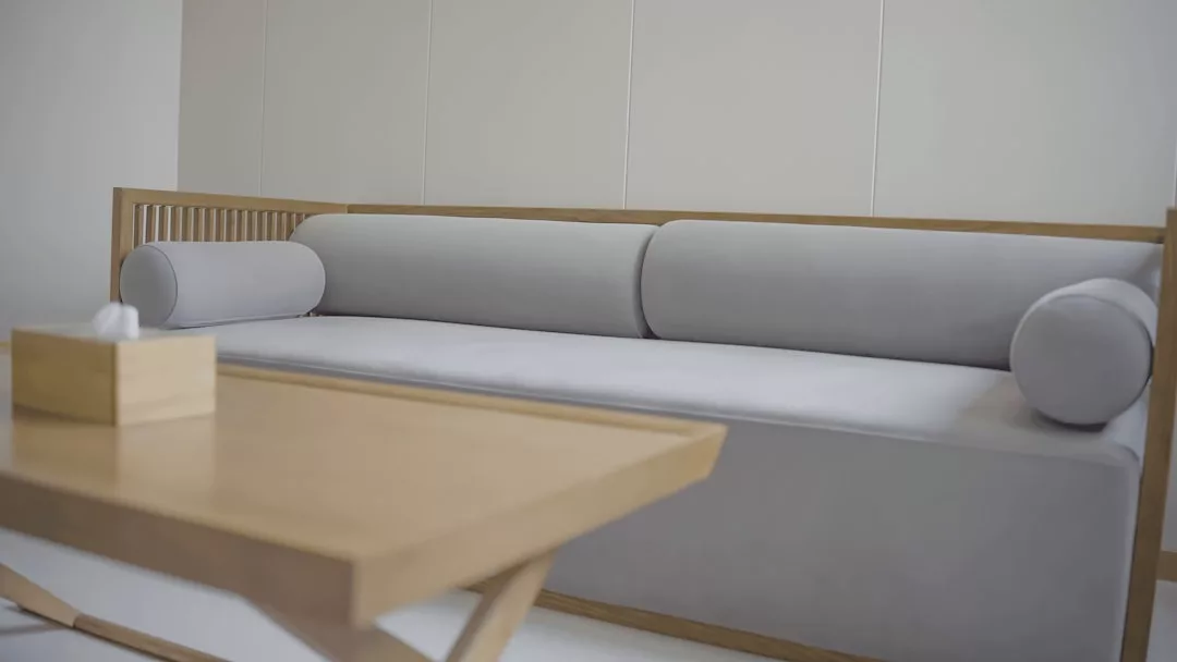 Minimalistisches Wohnzimmer im mallorquinischen Stil mit einem hellgrauen Polstersofa mit Holzarmlehnen, zwei zylindrischen Kissen und einem Couchtisch aus Holz mit einer Taschentuchbox.