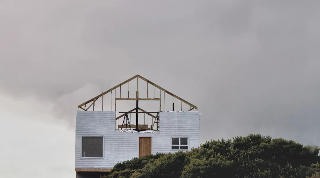 Ein teilweise fertiggestelltes oder verlassenes Haus, von dem nur das Dachgerüst sichtbar ist, hinter grünen Büschen unter einem bewölkten Himmel über Mallorca.