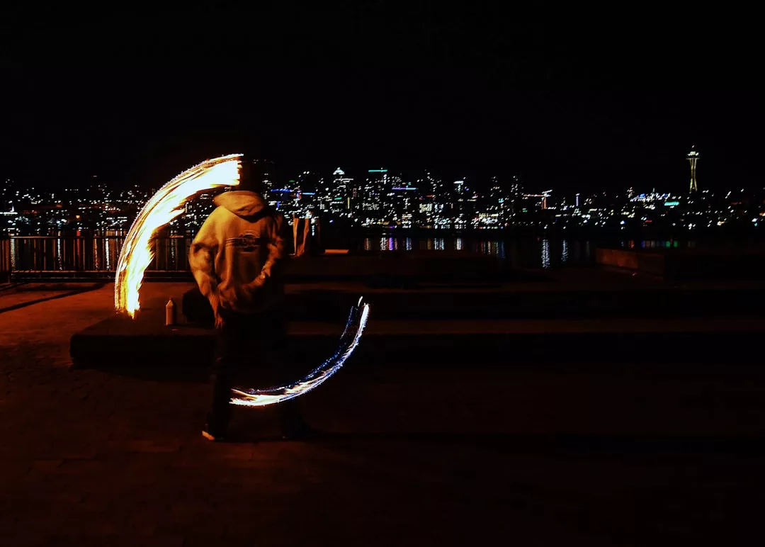 Eine Person führt nachts vor der Skyline einer Stadt Feuerwirbel auf, im Hintergrund spiegeln sich die beleuchteten Gebäude Mallorcas im Wasser.