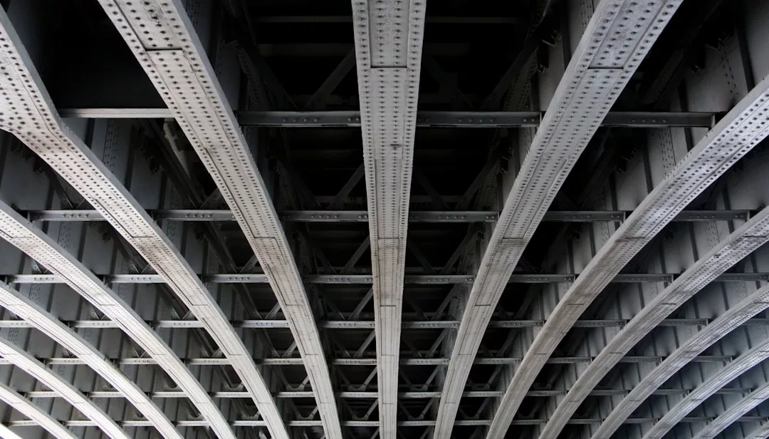 Unterseite einer Stahlbrücke auf Mallorca. Sie zeigt mehrere parallele Metallträger und Querverstrebungen, die ein gitterartiges Strukturmuster bilden.