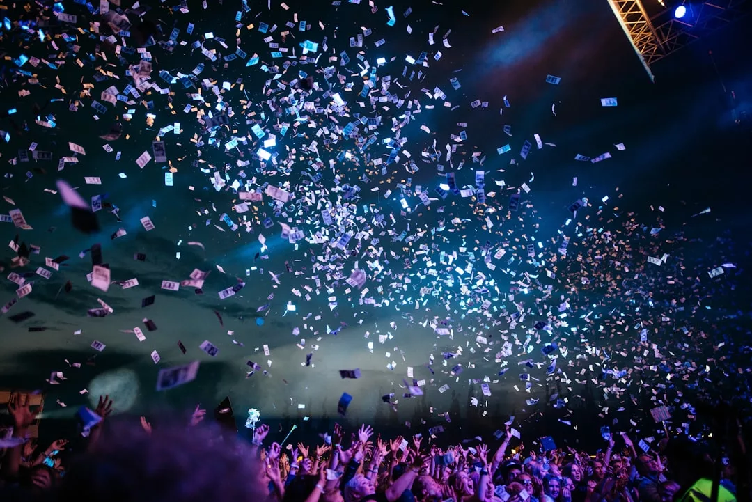 Bei einem Konzert oder einer Veranstaltung auf Mallorca streckt eine große Menschenmenge die Arme nach oben, während Konfetti von oben herabfällt und von Bühnenlichtern vor einem dunklen Himmel angestrahlt wird.
