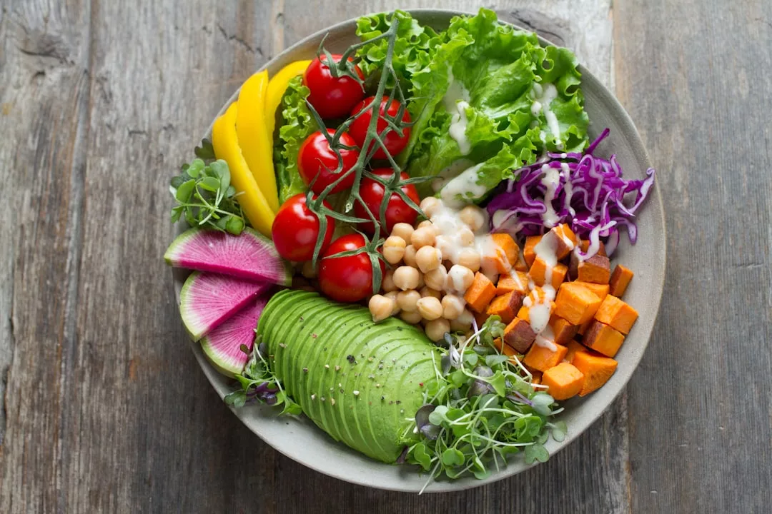 Eine farbenfrohe, von Mallorca inspirierte Schüssel mit verschiedenen frischen Gemüsesorten und Hülsenfrüchten wie Avocado, Tomaten, Kichererbsen, Süßkartoffeln, Salat, Kohl, Radieschen und Microgreens, alles mit Dressing beträufelt.