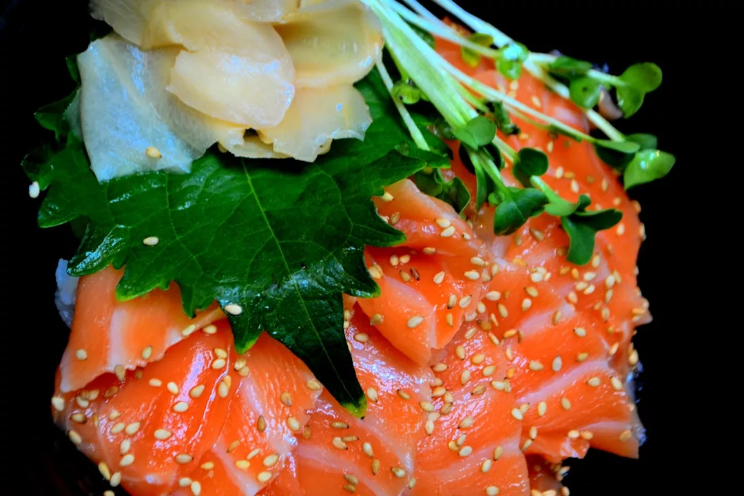 Eine Schüssel mit in Scheiben geschnittenem rohem Lachs, garniert mit Sesamkörnern, grünen Blättern, Microgreens und eingelegtem Ingwer – ein Hauch der frischen Aromen Mallorcas mit jedem Bissen.