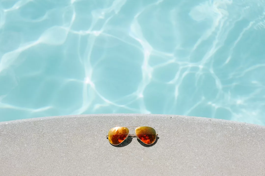 Eine Pilotenbrille liegt am Rand eines Pools auf Mallorca, im Hintergrund schimmert klares blaues Wasser.