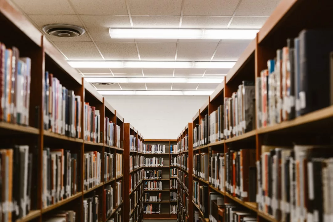 Reihen von Bücherregalen voller Bücher in einer Bibliothek, durch zwei Regale hindurch unter fluoreszierendem Deckenlicht betrachtet, rufen den ruhigen Charme eines Mallorca-Nachmittags hervor, an dem man verborgene literarische Schätze erkundet.