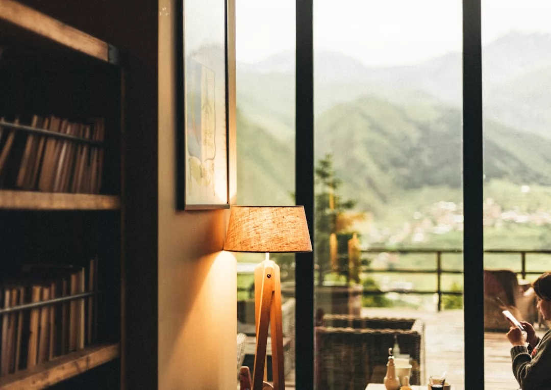Ein gemütlicher Raum mit einer Stehlampe, einem Bücherregal und Glastüren, die auf eine Terrasse mit atemberaubendem Blick auf die Berge Mallorcas führen.