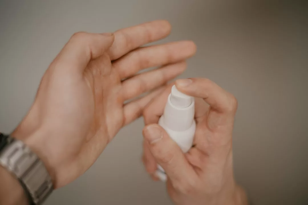 Eine Person hält eine weiße Sprühflasche und sprüht Flüssigkeit auf ihre offene Handfläche, vielleicht bereitet sie sich auf sonnendurchflutete Abenteuer auf Mallorca vor.