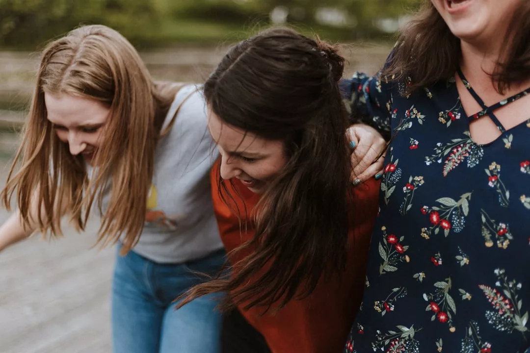 Drei Frauen stehen auf Mallorca dicht beieinander, lächeln und lachen im Freien und haben die Arme umeinander gelegt.