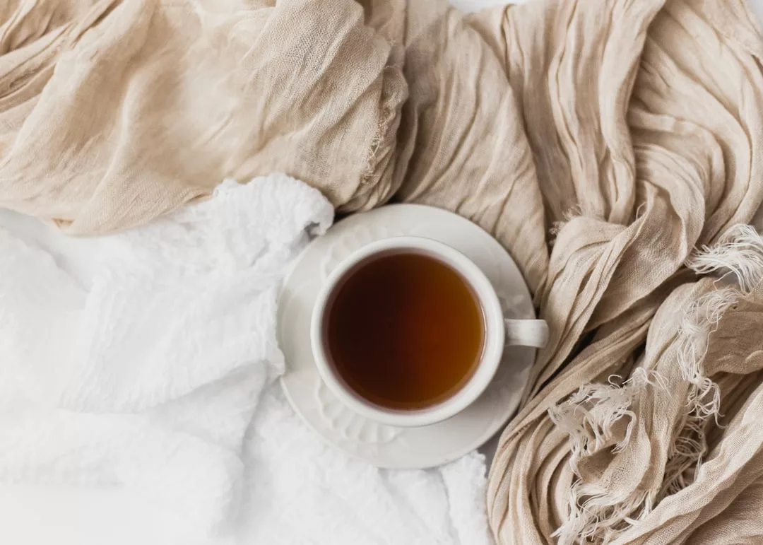 Eine weiße Tasse mit Tee steht auf einer passenden Untertasse, umgeben von beige-weißem strukturiertem Stoff, der an die entspannte Eleganz Mallorcas erinnert.