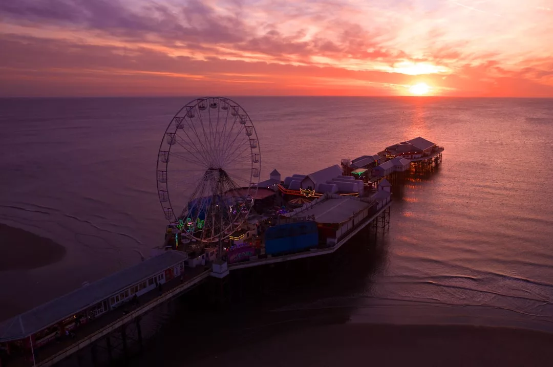Ein Küstenpier auf Mallorca mit einem Riesenrad und Gebäuden erstreckt sich bei Sonnenuntergang über ruhigem Wasser, der Himmel leuchtet orange und violett.
