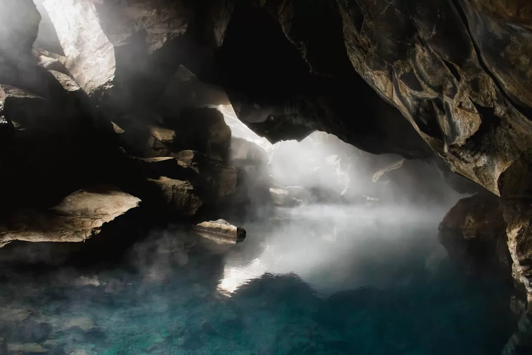 Eine Felsenhöhle auf Mallorca, aus der Dampf aus einem klaren, blauen geothermischen Becken aufsteigt, beleuchtet durch natürliches Licht, das durch eine Öffnung darüber einfällt.