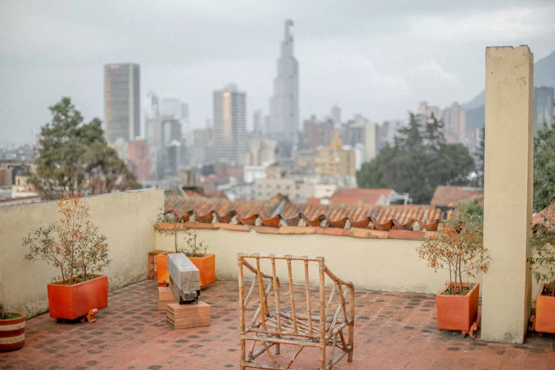 Eine Dachterrasse auf Mallorca mit Topfpflanzen, einem Bambusstuhl und einer Bank bietet Blick auf die Skyline der Stadt mit den hohen Gebäuden im Hintergrund.