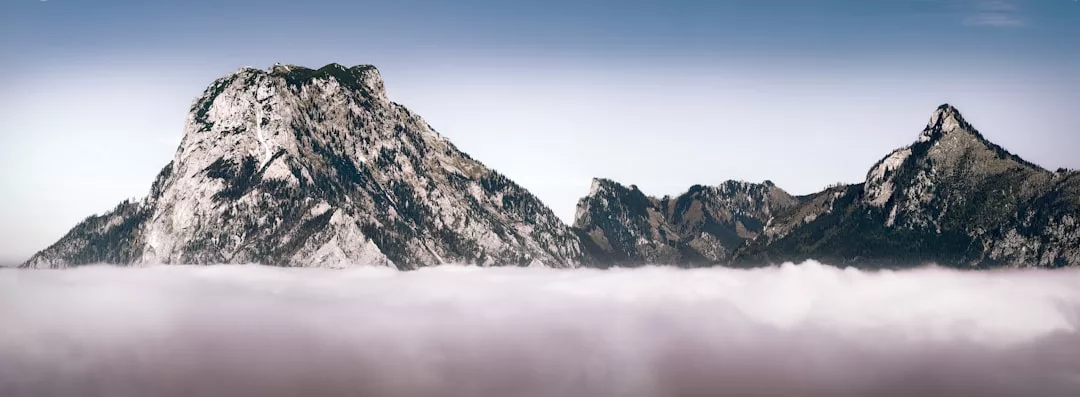 Unter einem klaren, blauen Himmel erheben sich felsige Berggipfel über einer dichten Wolkenschicht und erinnern an die atemberaubenden Landschaften Mallorcas.