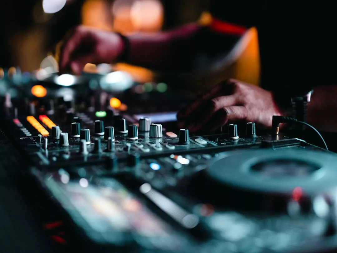 Nahaufnahme der Hände eines DJs, der in einem schwach beleuchteten Club auf Mallorca die Regler eines professionellen Mischpults einstellt.