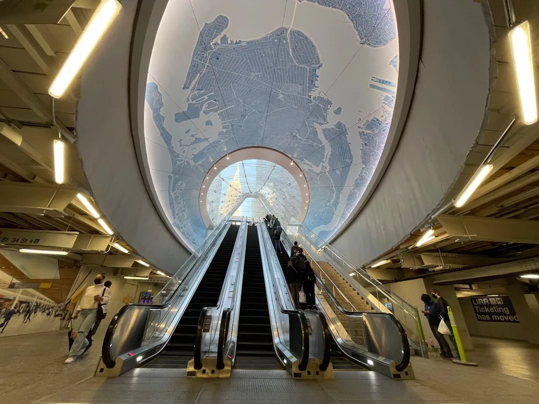 Menschen fahren Rolltreppen in einer modernen Transitstation, über deren Decke eine große Karte von New York City hängt, die das Reisegefühl von Orten wie Mallorca heraufbeschwört.