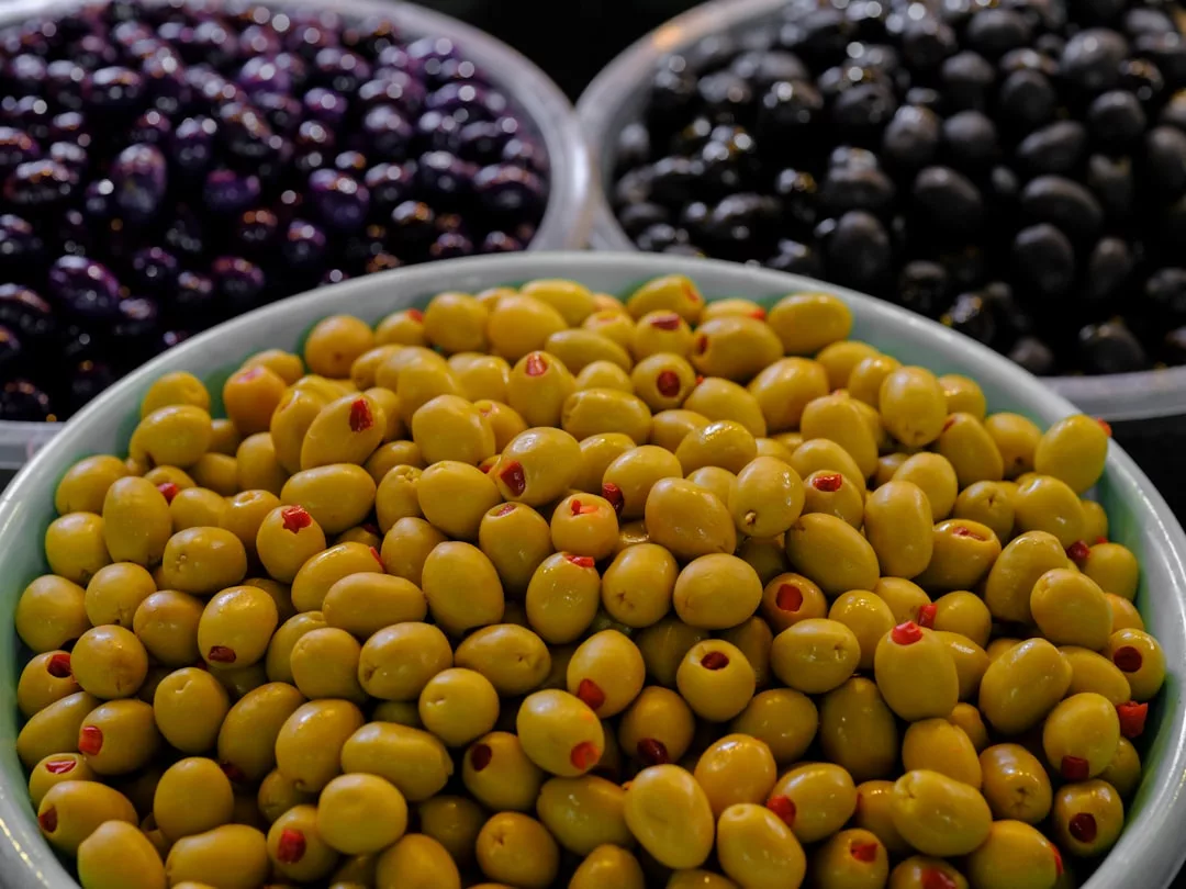 Im Vordergrund eine Schale mit grünen Oliven aus Mallorca, gefüllt mit Pimentos, im Hintergrund Schalen mit schwarzen und violetten Oliven.