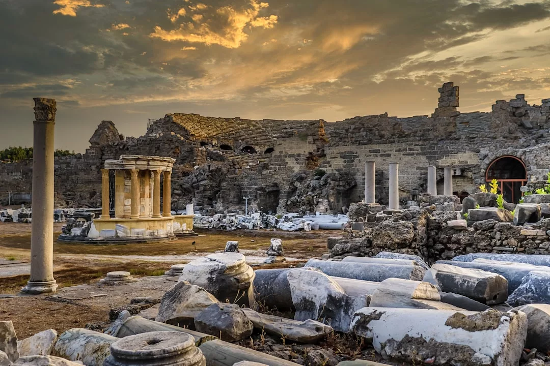 Antike Steinruinen und Säulen sind über eine historische Ausgrabungsstätte auf Mallorca verstreut, unter einem dramatischen, bewölkten Himmel bei Sonnenuntergang.