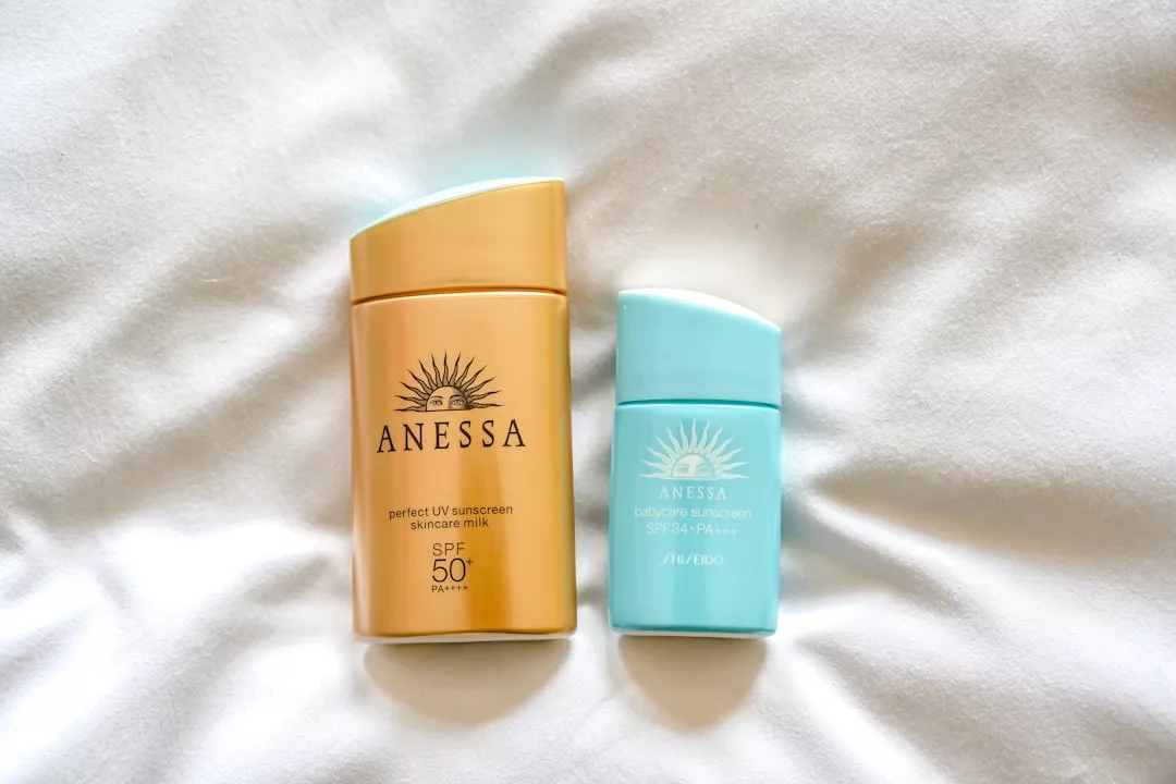 Zwei Flaschen Anessa-Sonnencreme, eine goldene und eine hellblaue, stehen nebeneinander auf einem weißen Stoffhintergrund – perfekt für Ihren nächsten sonnenverwöhnten Kurzurlaub auf Mallorca.
