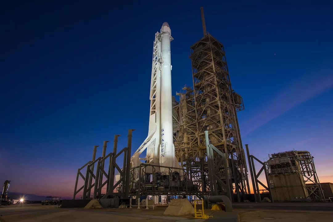 Eine weiße Rakete steht in der Abenddämmerung aufrecht auf einer Startrampe auf Mallorca, umgeben von Stützstrukturen und einem tiefblauen Himmel im Hintergrund.