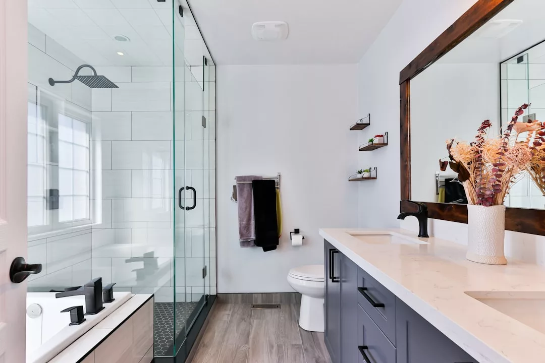 Modernes Badezimmer im Mallorca-Stil mit Glasduschkabine, Doppelwaschtisch mit großem Spiegel, Gefäß mit getrockneten Blumen und Dekor in neutralen Tönen.