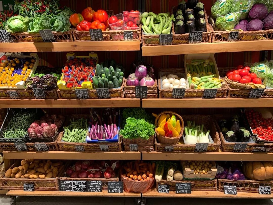 In den Regalen eines Lebensmittelladens auf Mallorca wird eine Vielfalt an frischem Gemüse angeboten, darunter Paprika, Gurken, Salat, Tomaten, Auberginen, Kartoffeln und Zwiebeln, alles mit Preisschildern versehen.