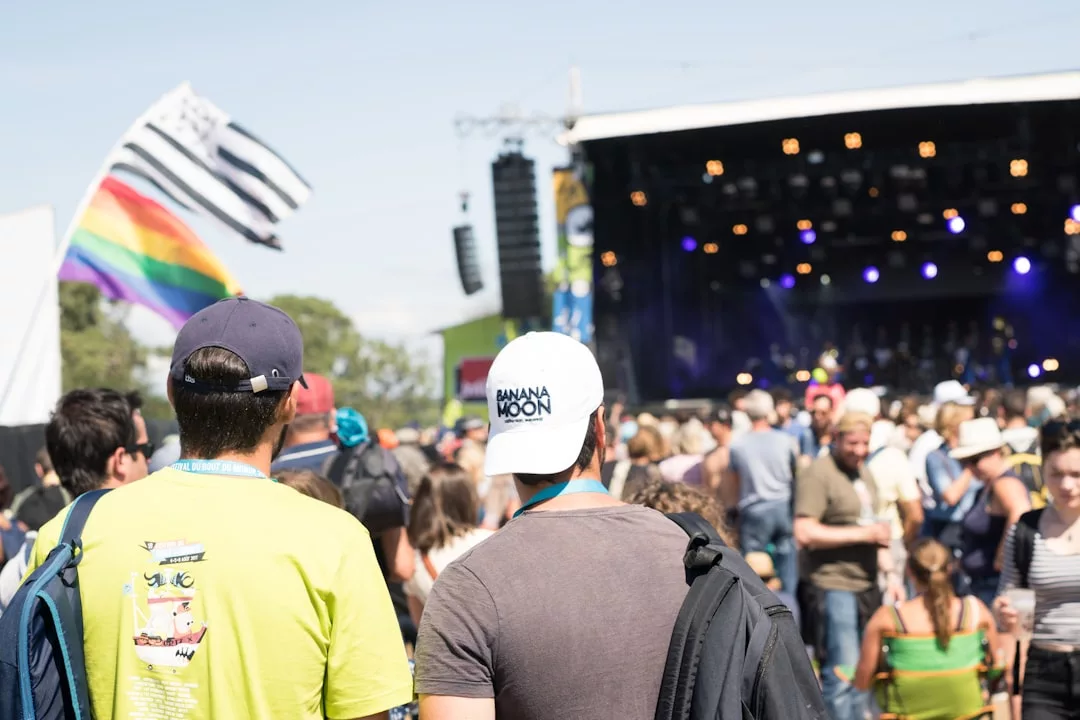 Eine Menschenmenge steht im Freien bei einem Musikfestival auf Mallorca, im Hintergrund ist eine Bühne zu sehen und in der Szene sind mehrere Flaggen zu sehen, darunter eine Regenbogenflagge.