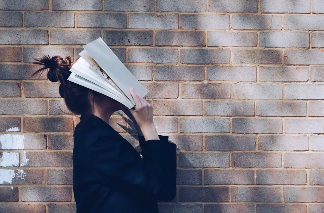 Eine Person steht auf Mallorca vor einer Backsteinmauer und hält ein offenes Buch vor ihr Gesicht, sodass ihre Gesichtszüge verdeckt sind.