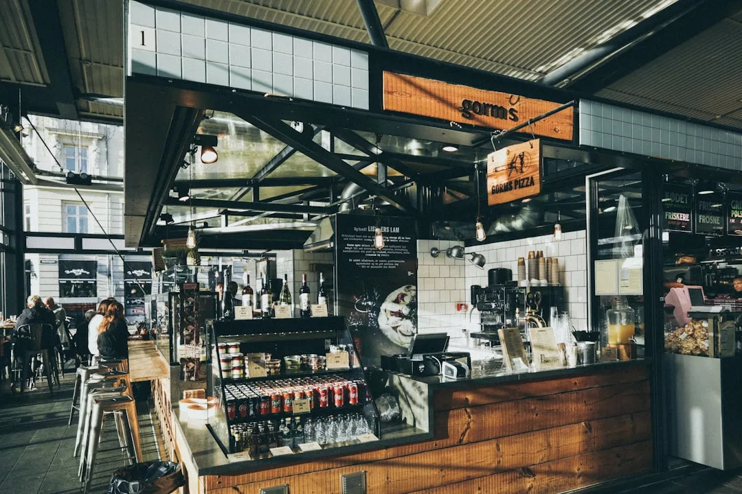 Ein moderner Imbissstand mit Holz- und Fliesenoberflächen, der Getränke, Snacks und eine von Mallorca inspirierte Pizzakarte in einer hellen Markthalle anbietet.