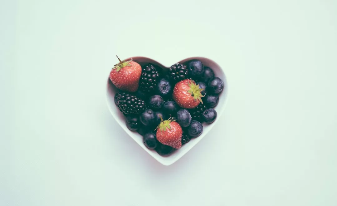 Eine herzförmige Schale gefüllt mit Erdbeeren, Brombeeren und Blaubeeren steht auf einem hellen, schlichten Hintergrund und erinnert an die frischen Aromen Mallorcas.