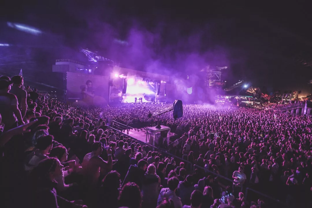 Eine große Menschenmenge besucht nachts ein Open-Air-Konzert auf Mallorca. Helle Bühnenlichter beleuchten die Künstler und violetter Dunst erfüllt die Luft.