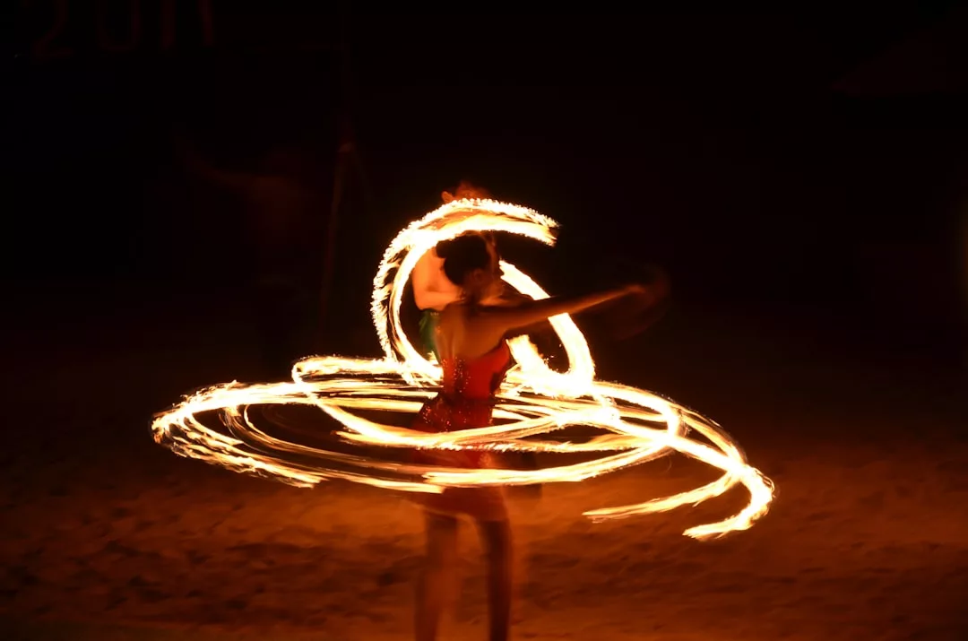 Ein Künstler auf Mallorca dreht mehrere Feuerreifen und erzeugt so kreisförmige Lichtspuren vor einem dunklen Hintergrund.