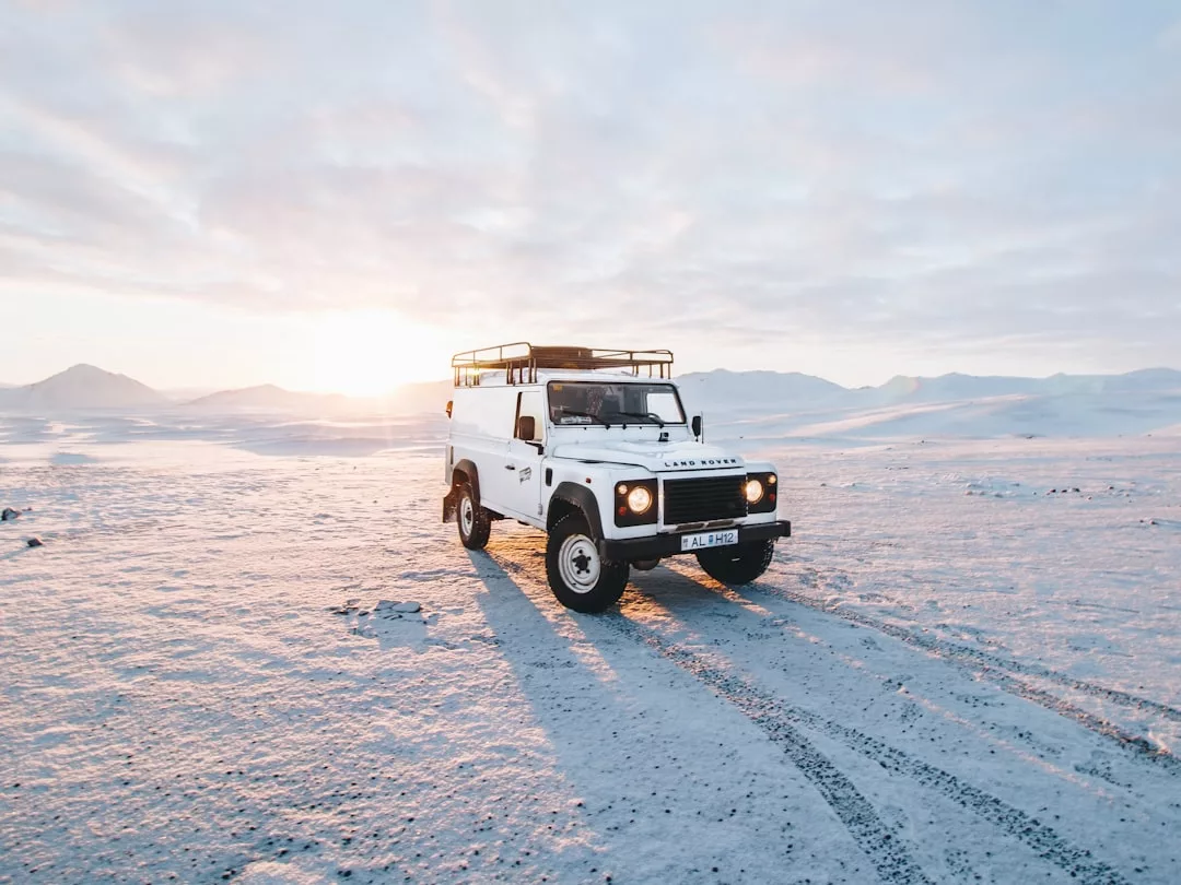 Ein weißer Land Rover Defender parkt in einer verschneiten Landschaft mit Bergen in der Ferne, die Sonne steht tief am Horizont und weckt einen abenteuerlichen Geist, der an Mallorcas raues Gelände erinnert.