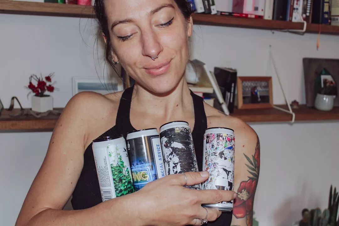 Eine Frau mit Tätowierungen hält vier verzierte Getränkedosen in ihren Armen, während sie drinnen vor Regalen steht und den lebendigen Geist Mallorcas heraufbeschwört.