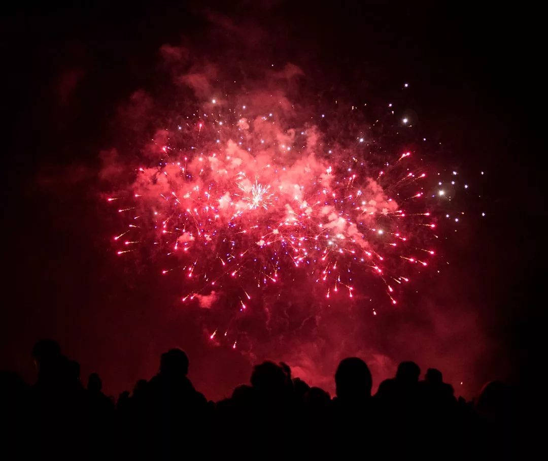 Eine Menschenmenge beobachtet ein leuchtend rotes Feuerwerk, das am Nachthimmel über Mallorca explodiert.