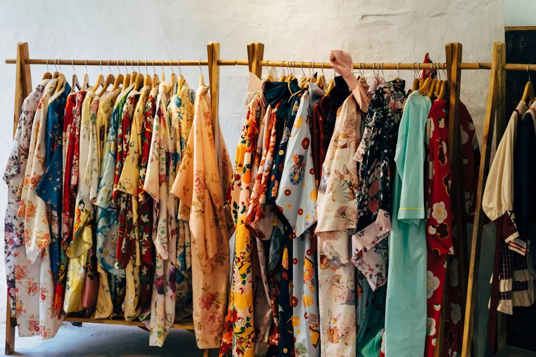 Auf einem hölzernen Kleiderständer hängen verschiedene bunte Kimonos und Roben mit Blumenmustern, die einer schlichten weißen Wand einen Hauch des lebhaften Stils Mallorcas verleihen.
