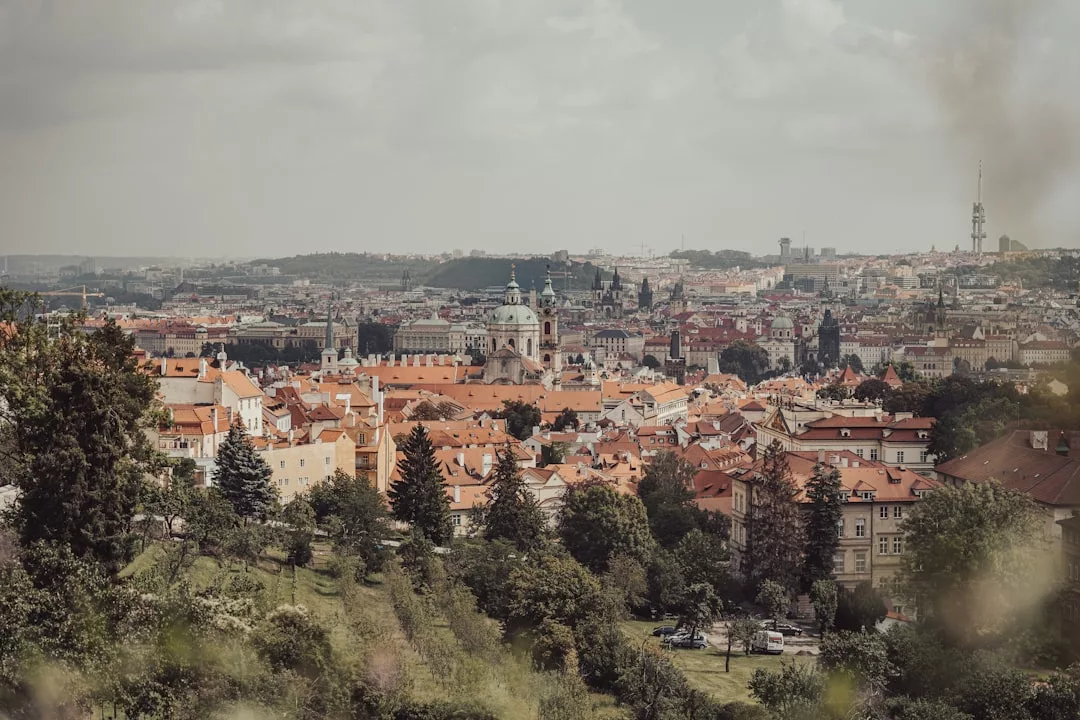 Stadtansicht von Prag mit Gebäuden mit roten Dächern, Kirchenkuppeln und grünen Bäumen unter einem bewölkten Himmel, die einen Charme hervorruft, der an die malerischen Städte Mallorcas erinnert.