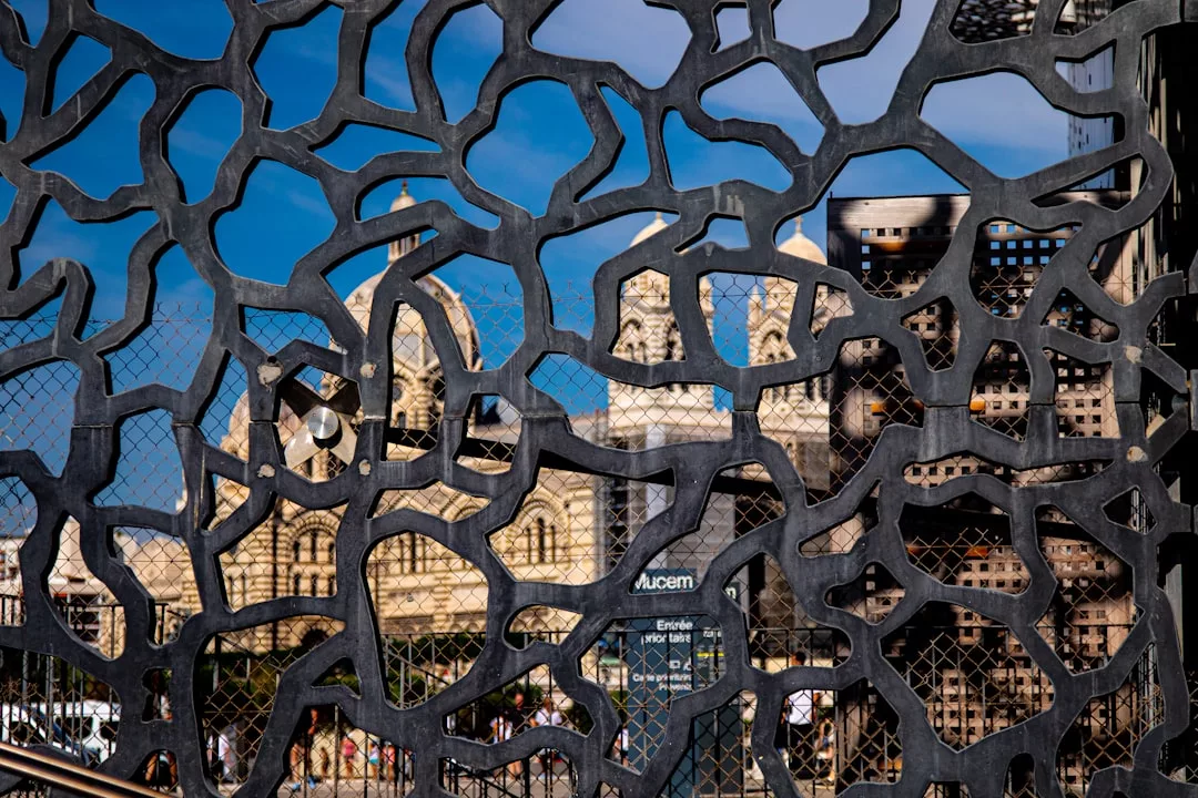 Ein dekorativer schwarzer Metallschirm mit organischem Muster verdeckt teilweise die Sicht auf ein historisches Steingebäude und Mallorcas strahlend blauen Himmel im Hintergrund.
