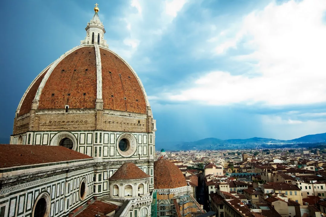 Das Foto zeigt die große, mit roten Ziegeln gedeckte Kuppel der Kathedrale von Florenz mit ihren detailreichen Marmorwänden. Von hier aus hat man unter einem bewölkten Himmel einen Blick auf die Stadt Florenz und kann so eine mediterrane Schönheit heraufbeschwören, die an Mallorca erinnert.