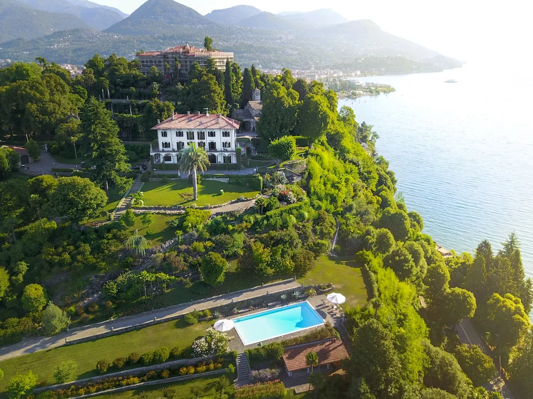 Eine große Villa auf Mallorca mit angelegten Gärten und einem Swimmingpool liegt auf einem Hügel mit Blick auf einen See und Berge im Hintergrund.